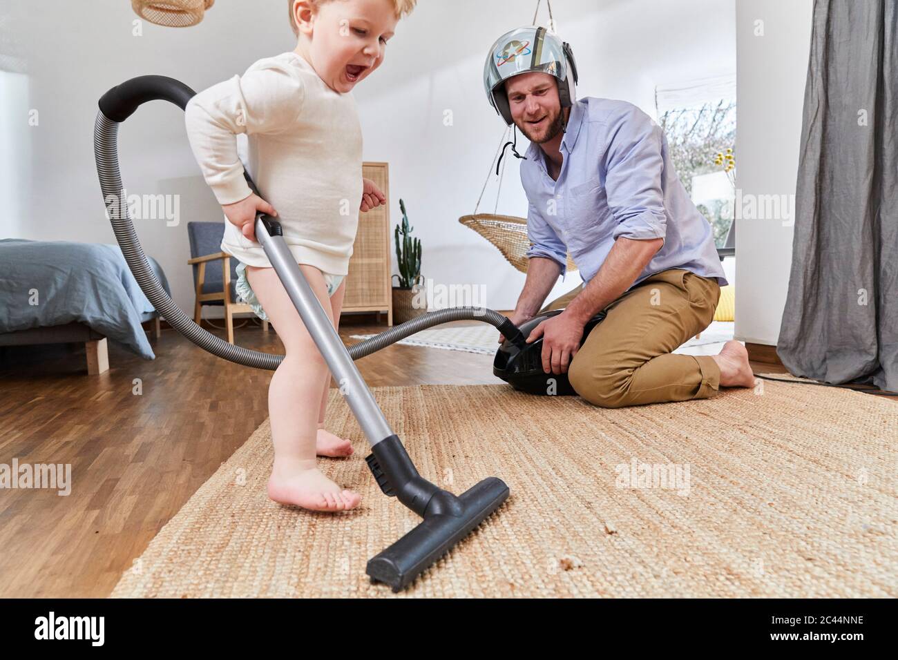 Niedlicher Baby Junge Reinigungsteppich mit Staubsauger vom Vater im Wohnzimmer zu Hause Stockfoto