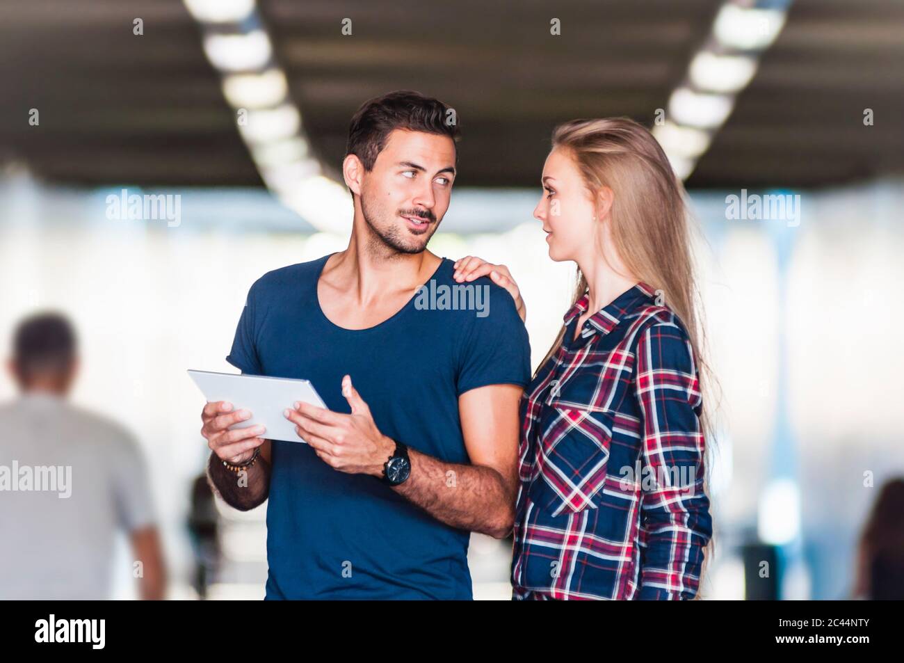 Porträt eines jungen Paares mit digitalem Tablet, das in einer Unterführung steht und sich anschaut Stockfoto