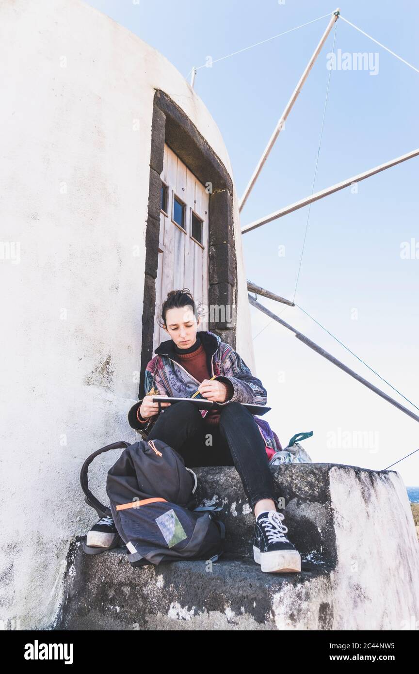 Junge Frau, die in einem Gebäude mit Buch und Bleistift sitzt, Corvo, Azoren, Portugal Stockfoto