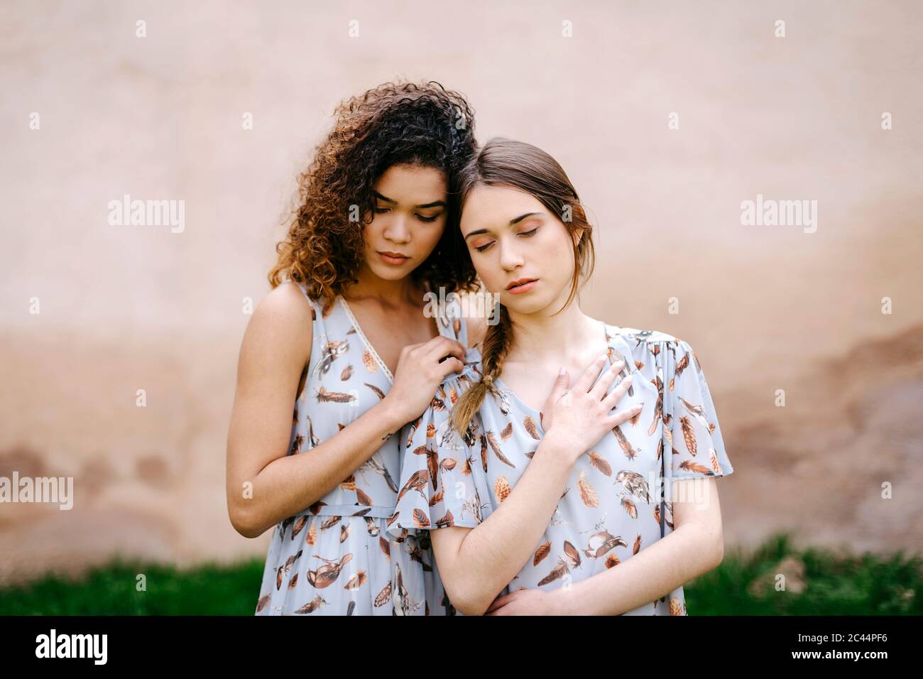 Liebevolle Schwestern mit geschlossenen Augen umarmt, während sie gegen alte Mauer stehen Stockfoto