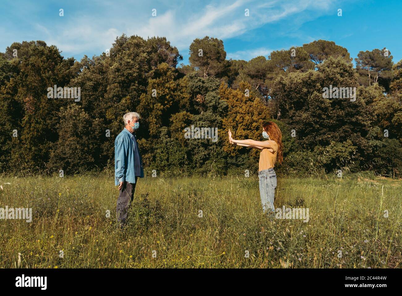 Frau und älterer Mann mit Masken stehen auf der Wiese, halten Sicherheitsabstand Stockfoto