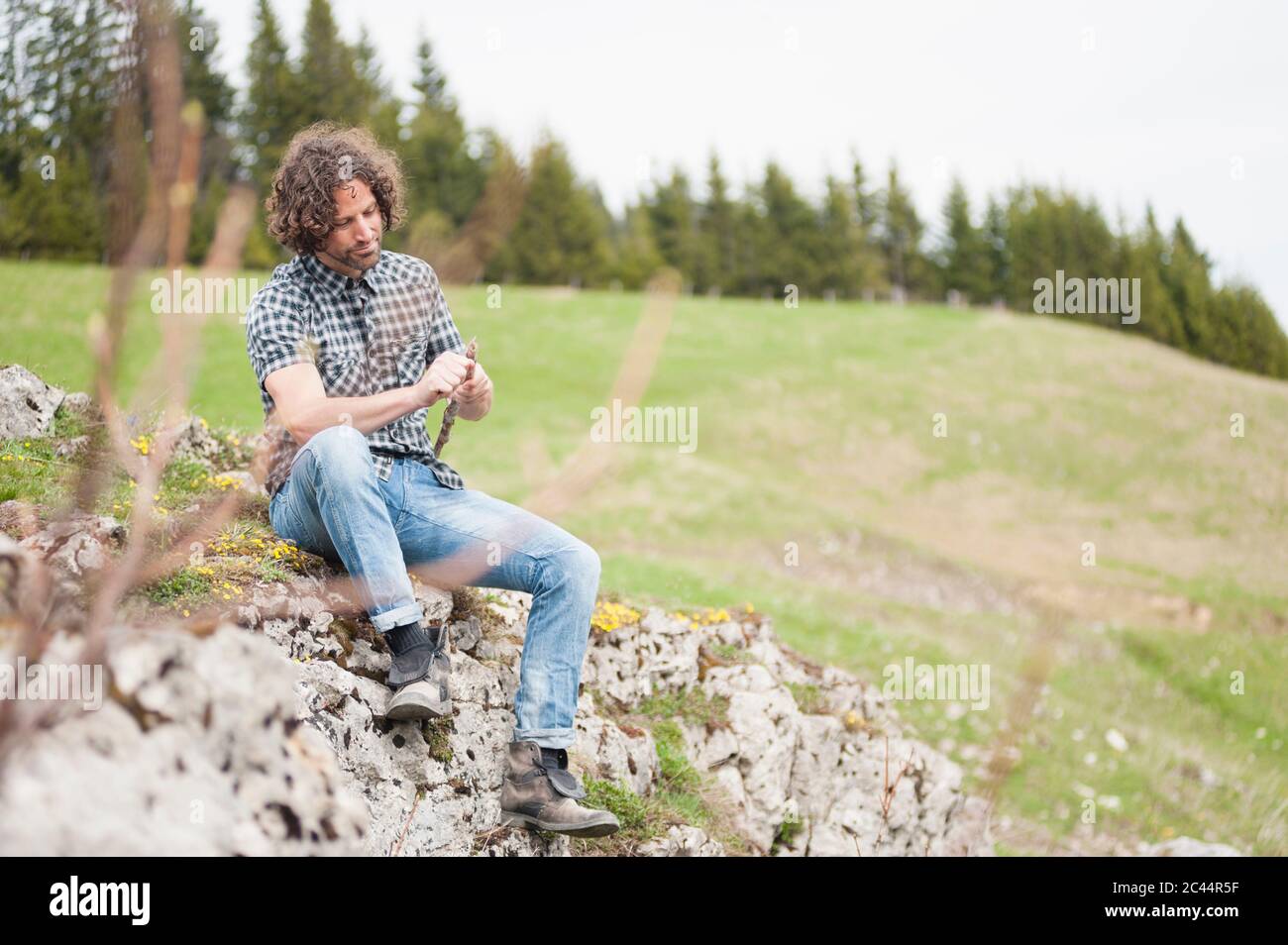 Mann hält Stock, während er auf Felsformation sitzt Stockfoto