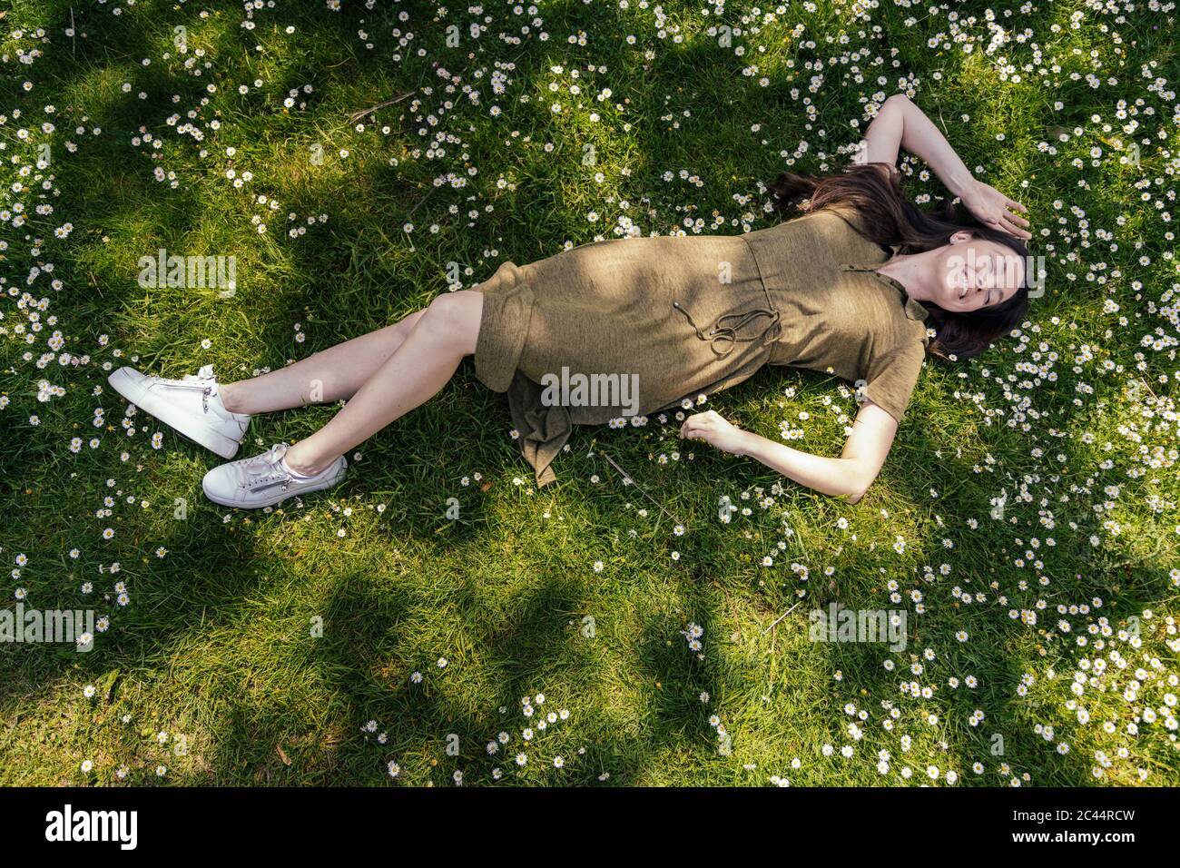 Frau genießt ihre Freizeit, während sie auf Gras mit Gänseblümchen liegt Stockfoto