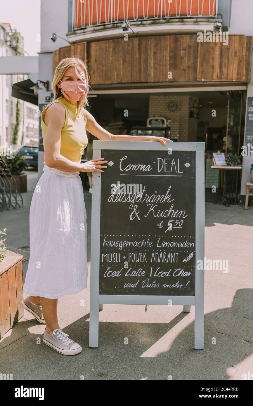 Cafe-Besitzer trägt Gesichtsmaske Entsendung eines Boards mit Corona Sonderangebote Stockfoto