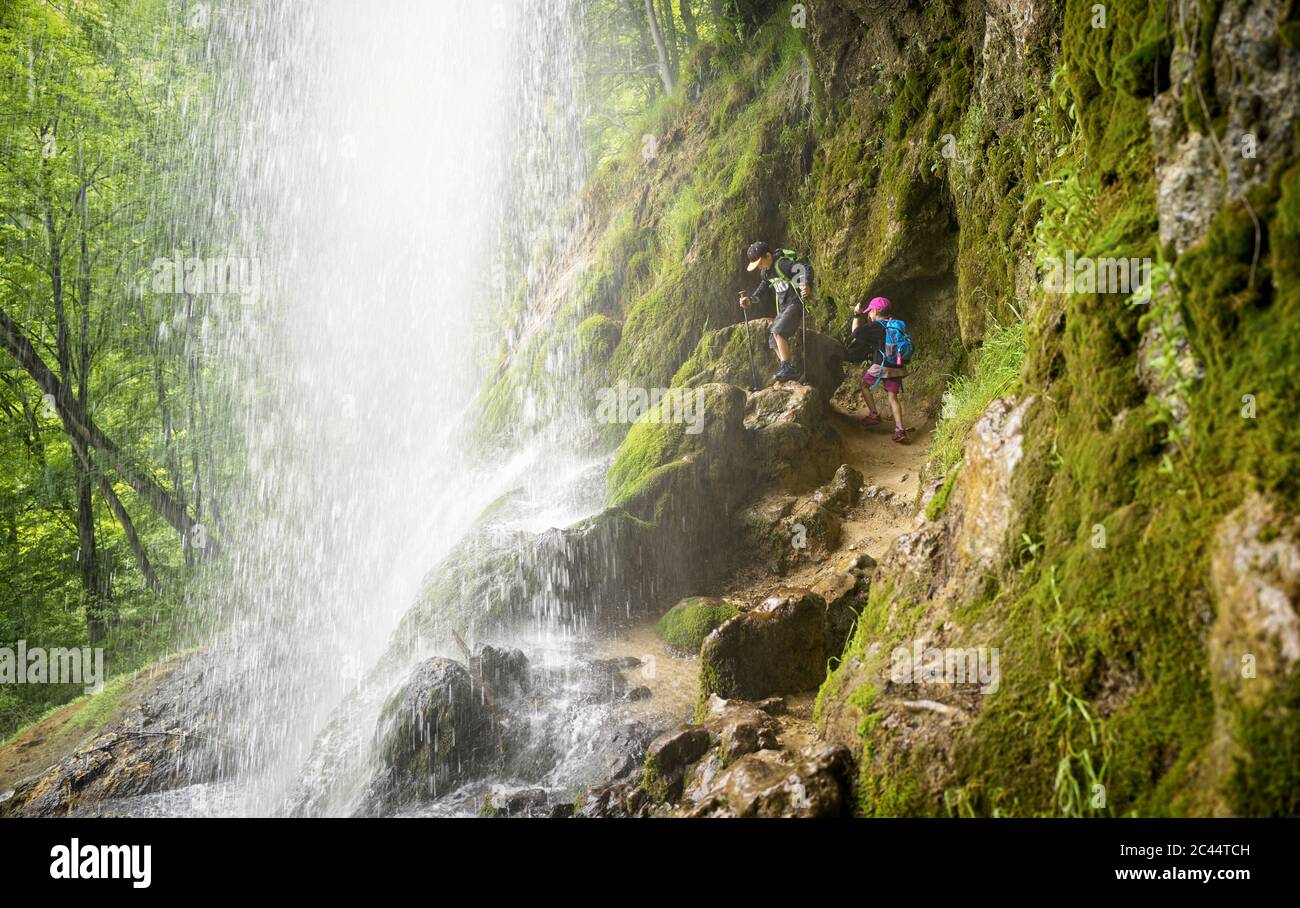 Junge und Mädchen wandern auf Felsformation unter Urach Wasserfall im Wald Stockfoto