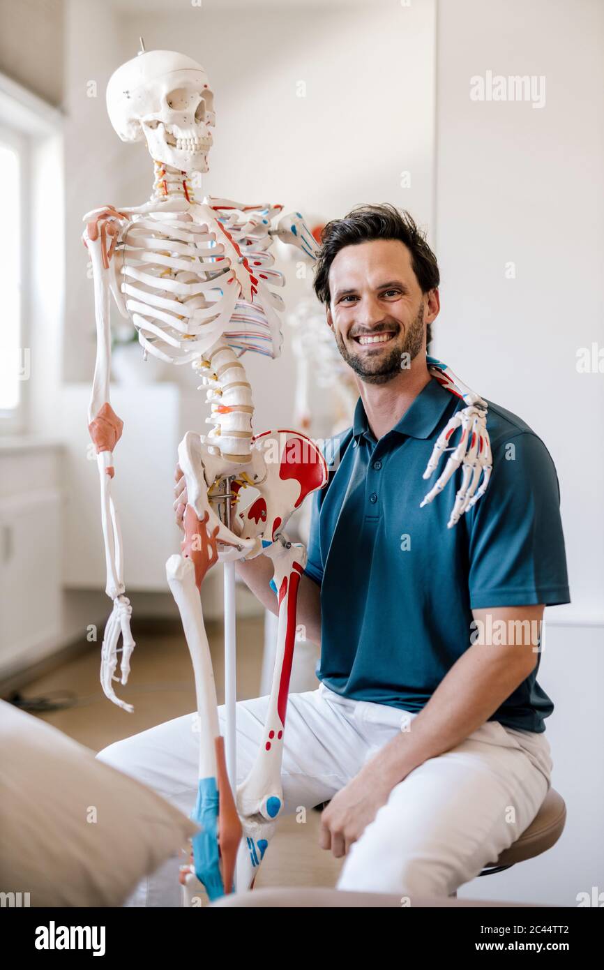 Physiotherapeut sitzt in der Praxis mit Skelettarm um seine Schulter Stockfoto