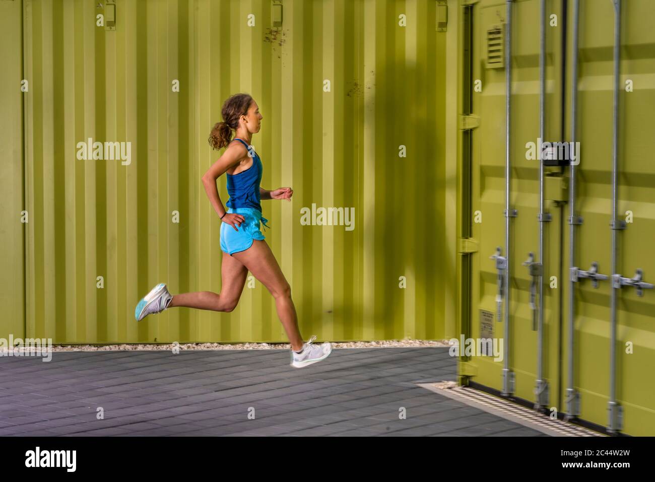 Junge Frau joggen auf bürgersteig vor Cargo Container Stockfoto