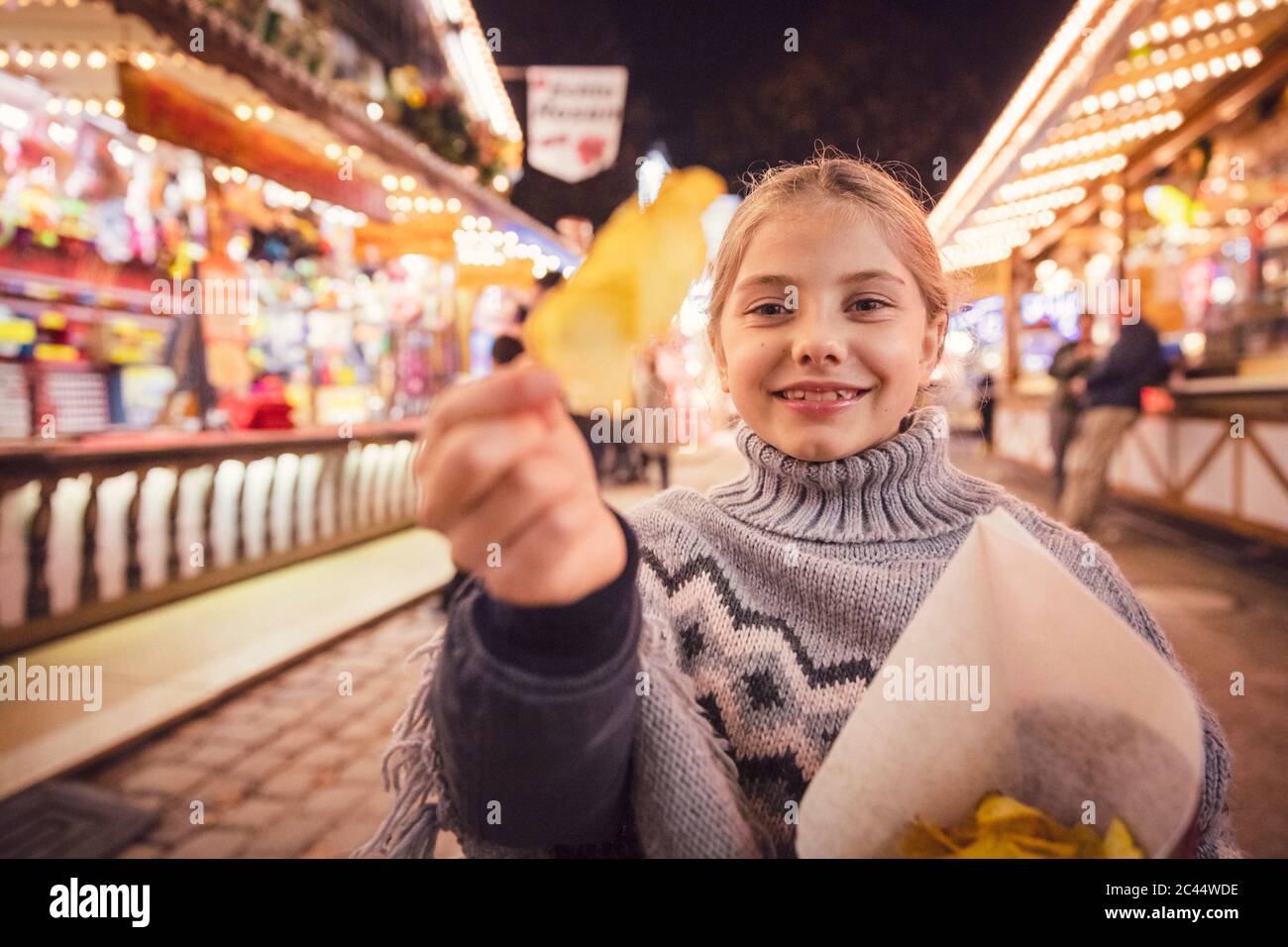 Portrait von lächelndem Mädchen, das Kartoffelchip an Karneval in der Stadt während der Nacht isst. München, Deutschland Stockfoto