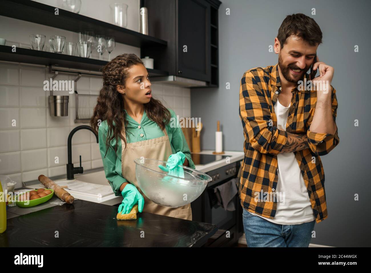 Junge multiethnische Paare putzt ihre Küche. Der Mann ist faul und die Frau ist wütend. Stockfoto