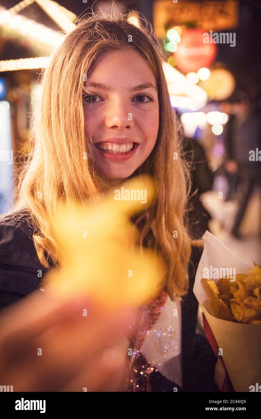 Portrait von lächelnd blonde Mädchen essen Kartoffel Chip an Karneval in der Stadt während der Nacht. München, Deutschland Stockfoto