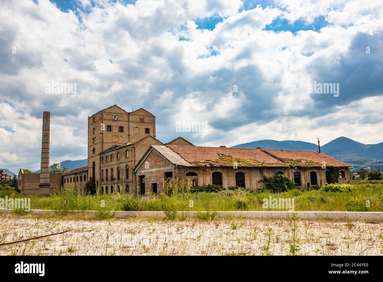 Eine alte stillgelegte Fabrik, verlassen und in Ruinen, mit einem zertrümmerten Dach und einem Kamin. Hohes Unkraut dringt in das Gebäude ein. Konzept des wirtschaftlichen Bankrotts. Clo Stockfoto