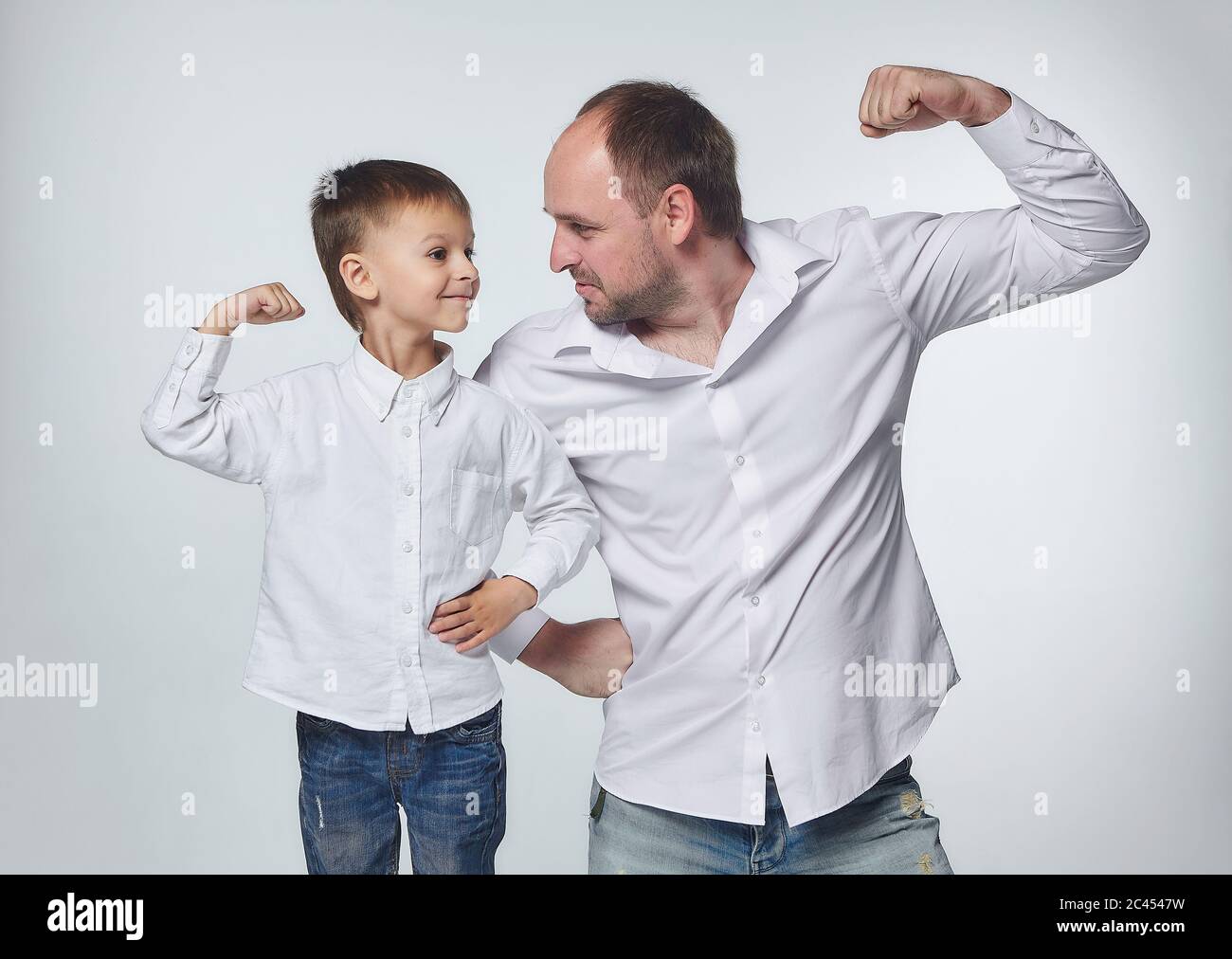 Vater und Sohn zeigen die Stärke ihrer Bizeps. Vaterschaft, Psychologie der Beziehungen.Studio, White back Stockfoto
