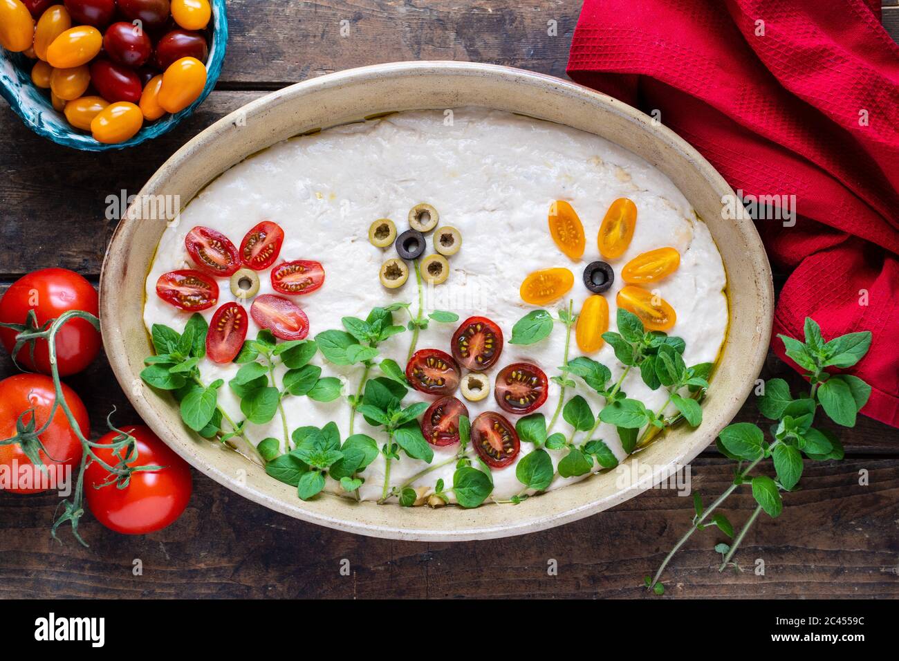 Hausgemachter Teig für köstliche, italienische Focaccia. Die Dekoration besteht aus Kirschtomaten, Oliven und frischen Kräutern. Stockfoto