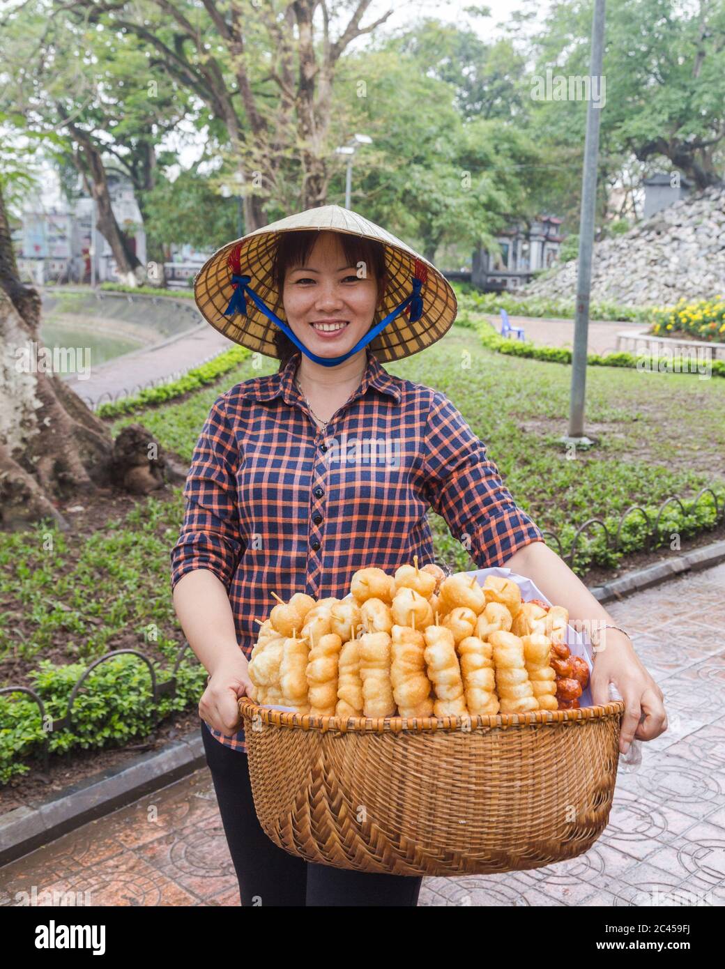 HANOI, VIETNAM, 19. MÄRZ 2017: Eine einheimische Dame in Hanoi verkauft süße Leckereien. Die Dame trägt einen traditionellen Kegelhut, der auf Vietnam üblich ist Stockfoto