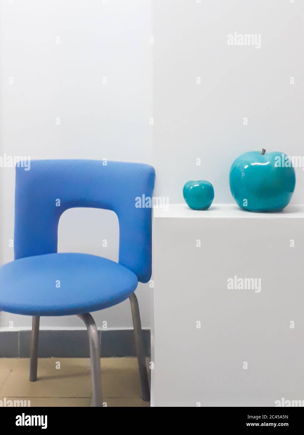 Details der Innenausstattung - eine weiße Wand, Bürostühle und zwei Keramik-Äpfel in türkisfarbener Farbe. Stockfoto