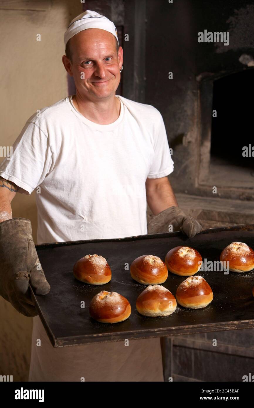 Lächelnder Bäcker hält ein Backblech mit Brötchen Stockfoto