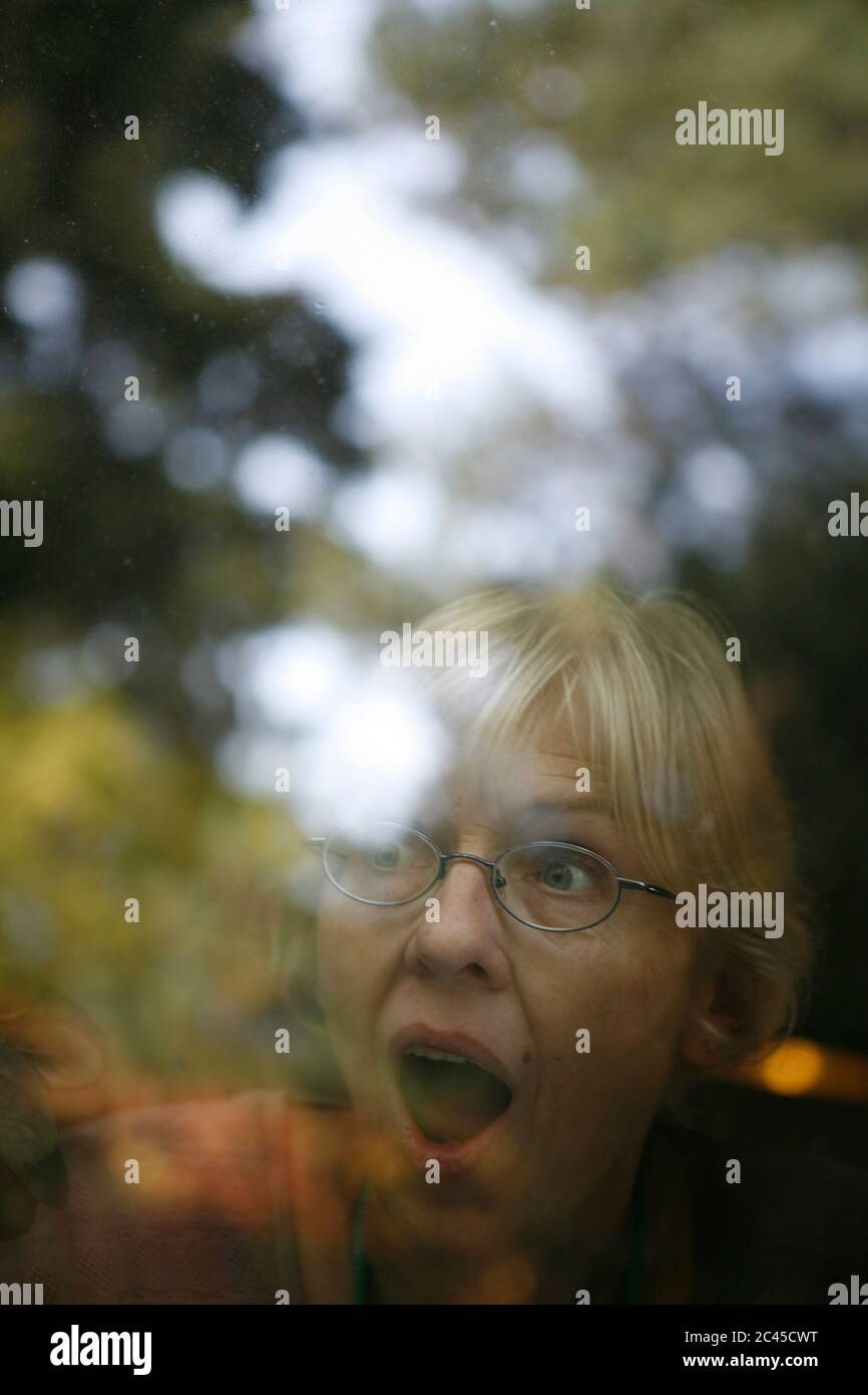 Überrascht ältere Frau schaut aus dem Fenster Stockfoto
