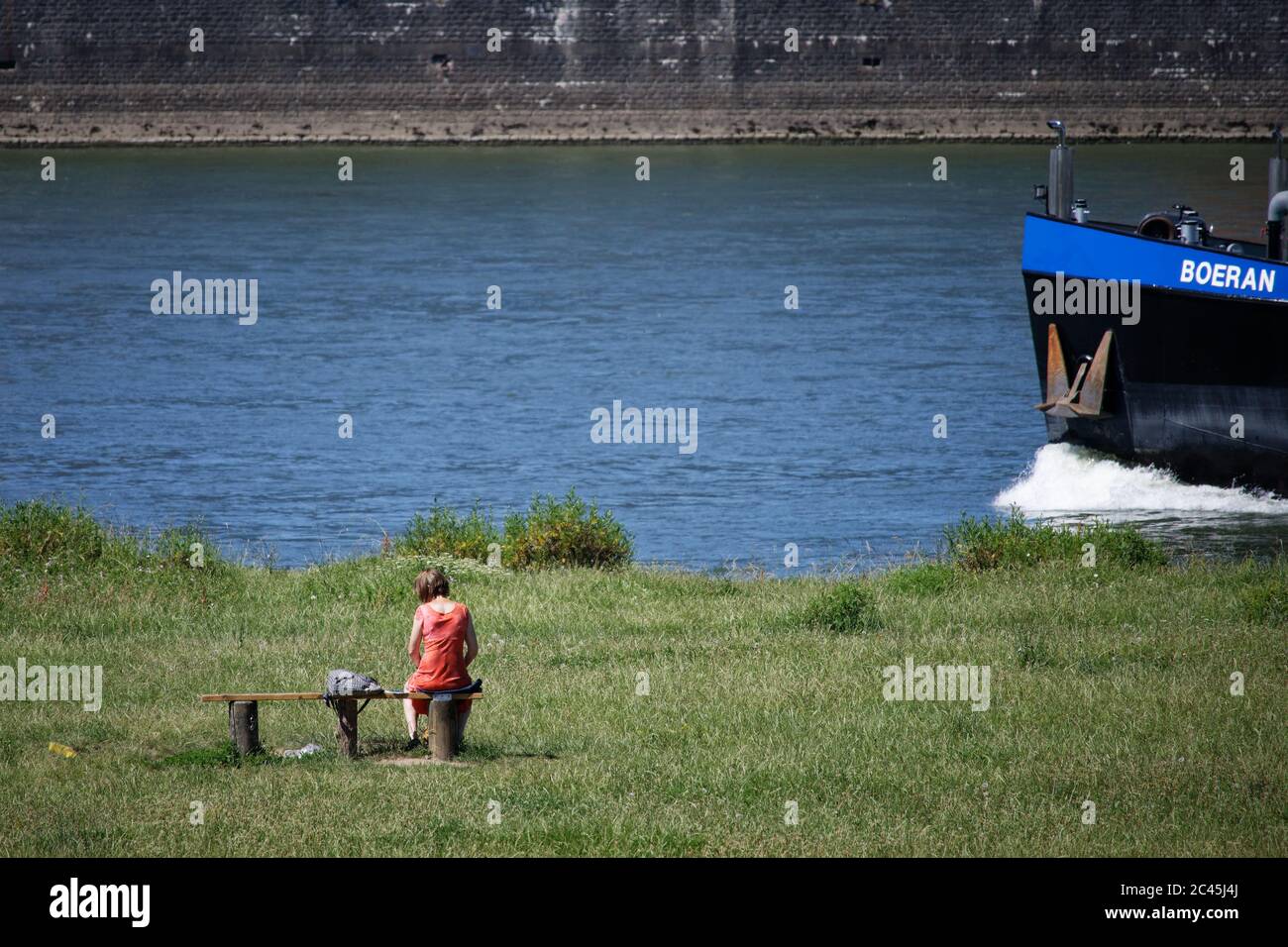 Köln, Deutschland. Juni 2020. Eine Frau genießt die Sonne auf den Pollerwiesen am Rheinufer, wenn ein Frachtschiff vorbeifährt. Quelle: Henning Kaiser/dpa/Alamy Live News Stockfoto