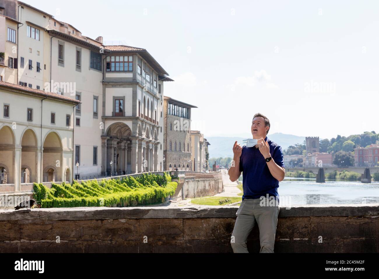 Mann mit Gesichtsmaske, der während der Corona-Virus-Krise allein auf der Brücke über den Fluss Arno in Florenz stand. Stockfoto