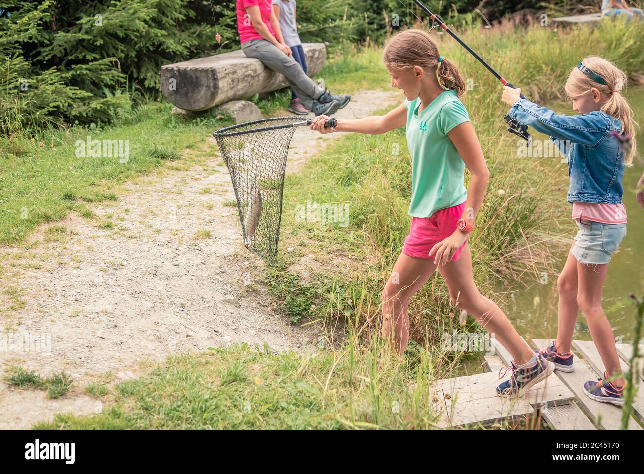 Zwei junge Mädchen halten Angelrute und Fischernetz mit gefangenen Fischen Stockfoto