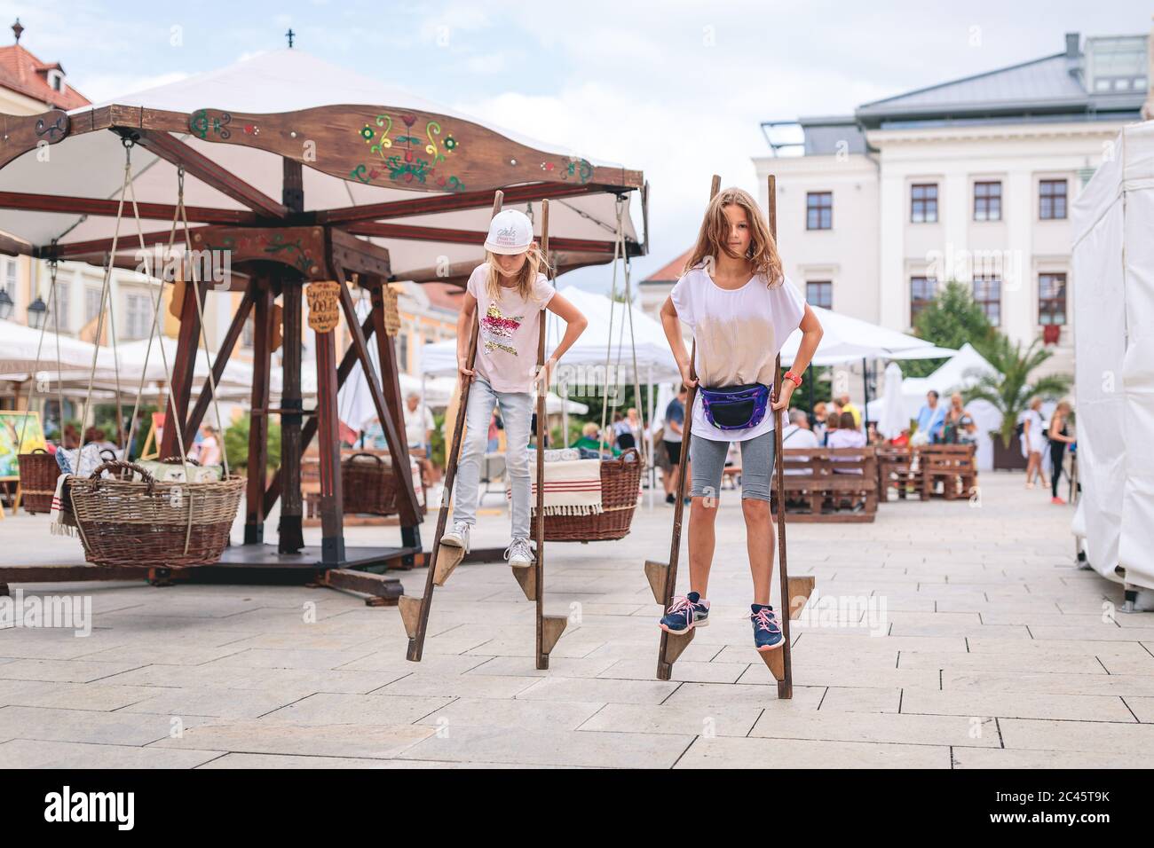 Zwei junge Mädchen, die während des Stadtfestes auf Stelzen spazieren, Dorfmesse Stockfoto