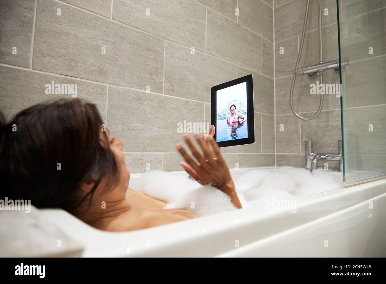 Frau sitzt in der Badewanne, mit Schaumbad und mit digitalen Tablette während Coronavirus Krise. Stockfoto