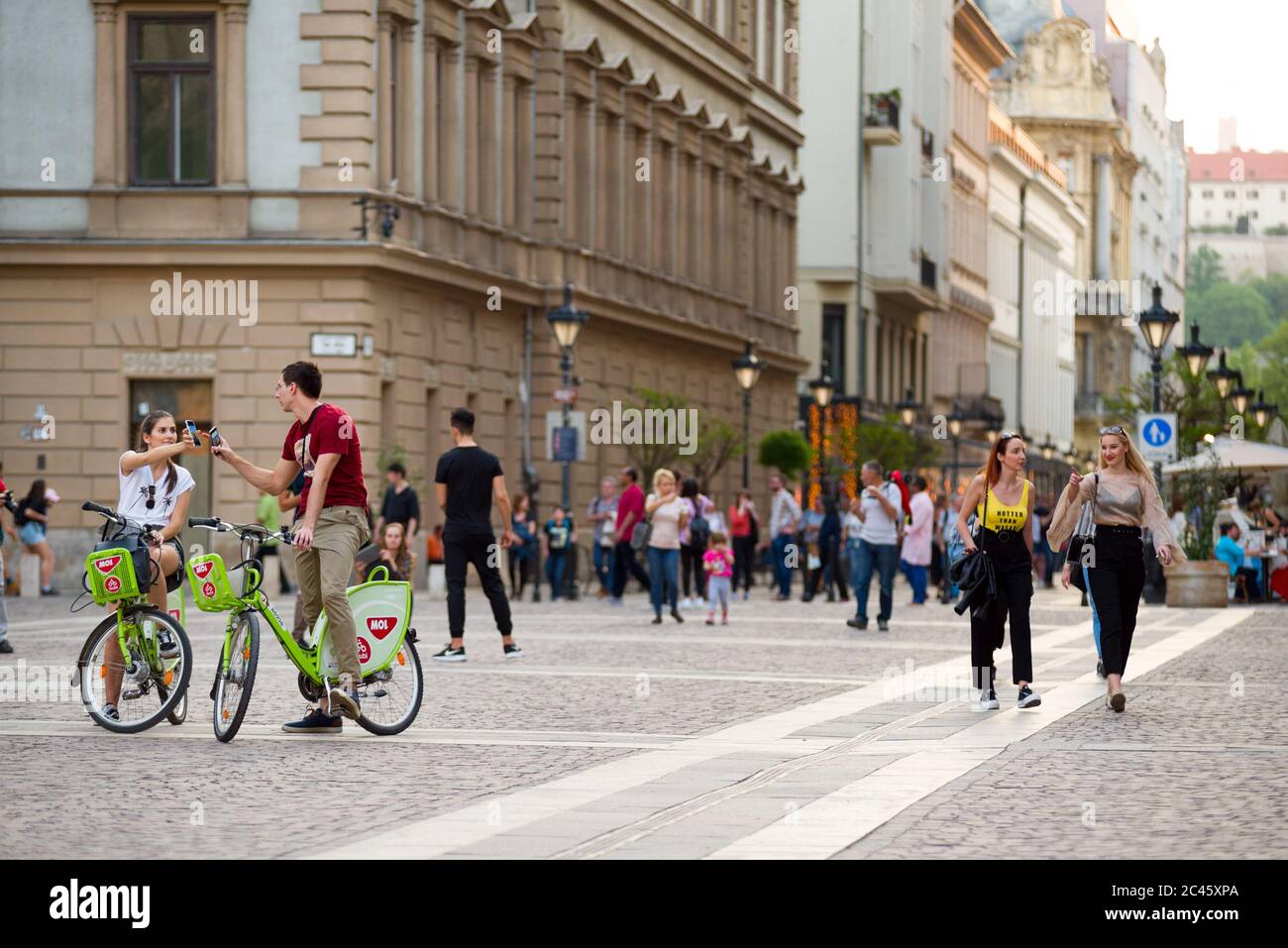 Junge Fahrradfahrer zeigen sich gegenseitig ihre Handy-Bildschirme gegen alte Gebäude der Innenstadt von Budapest Stockfoto