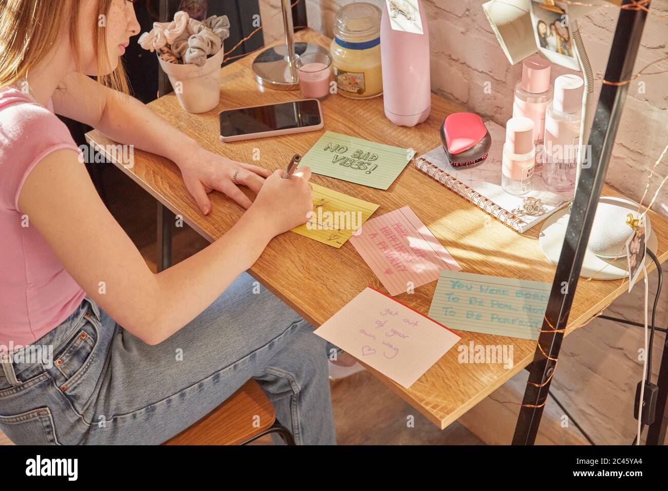 Teenager-Mädchen sitzt in ihrem Zimmer an einem Schreibtisch, schriftlich motivierende Zitate auf Karten. Stockfoto