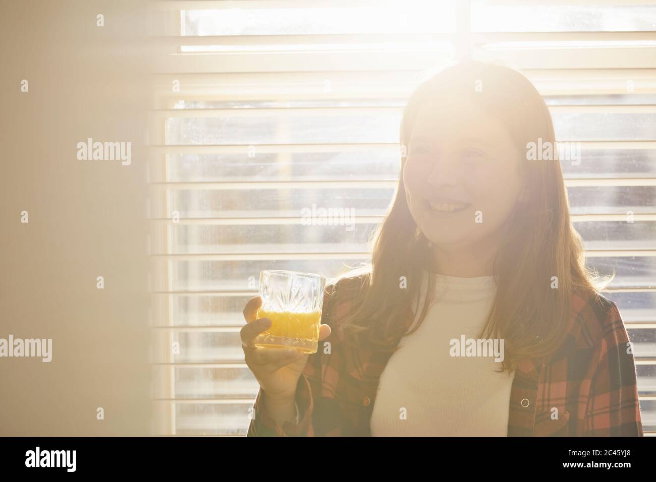 Teenager Mädchen, das vor dem Fenster steht und ein Glas Orangensaft hält. Stockfoto