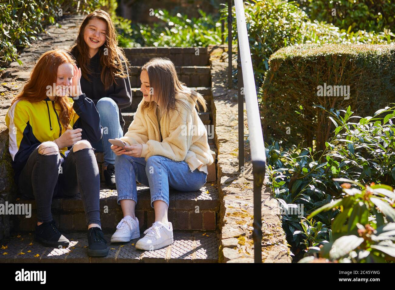 Drei Teenager Mädchen sitzen draußen auf der Treppe, Handy zu überprüfen. Stockfoto