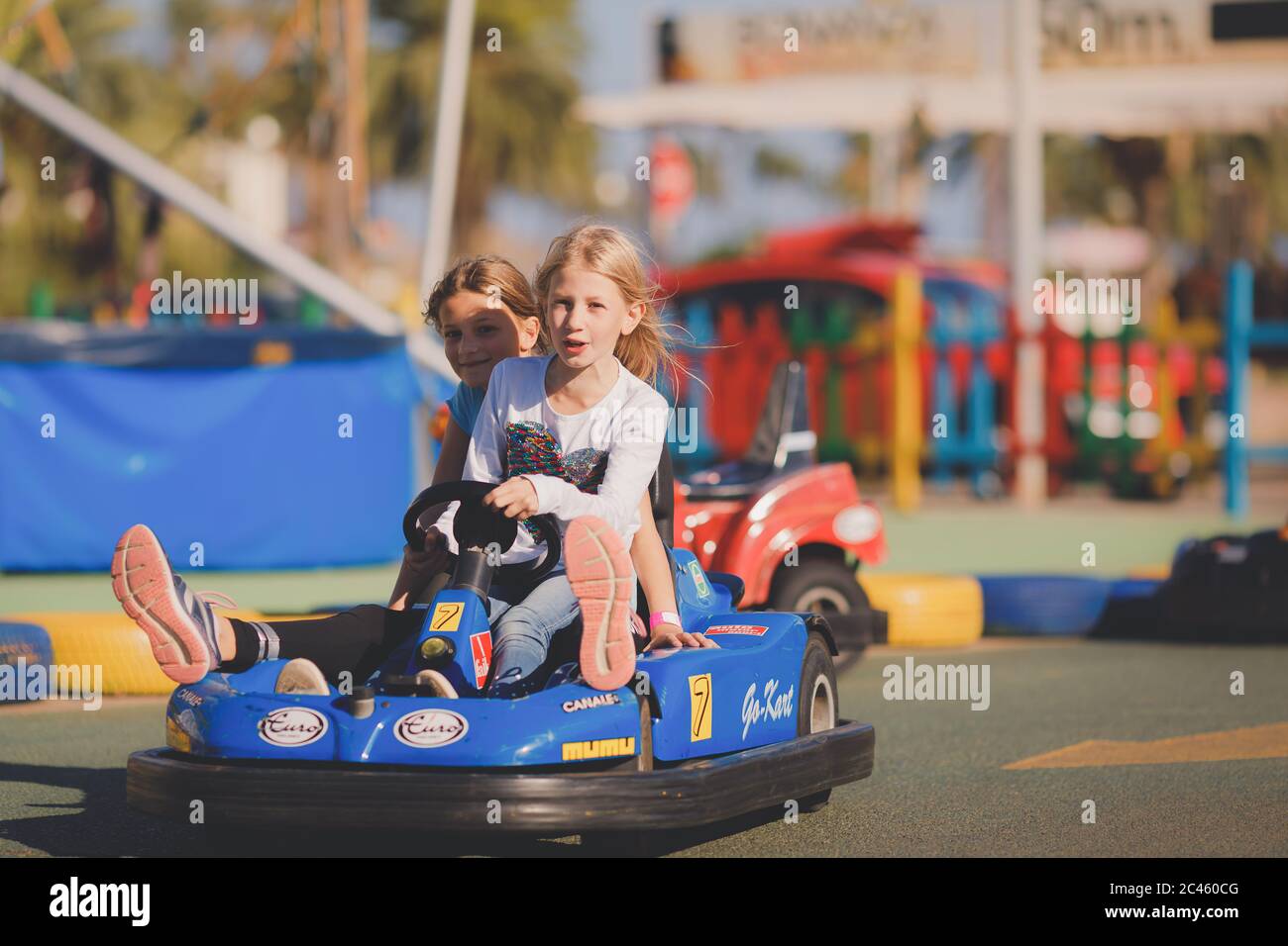 Junge Mädchen, die an einem sonnigen Tag in einem elektrischen Spielzeugauto in einer Küstenregion fahren Stockfoto