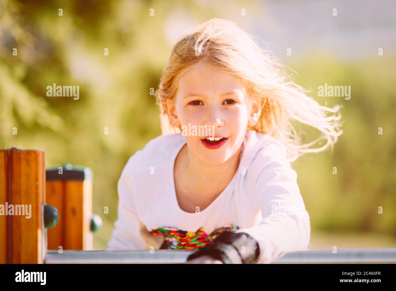 Portrait eines niedlichen Mädchens, Grundschulalter, mit blonden Haaren, die im Wind auf dem Spielplatz fliegen Stockfoto