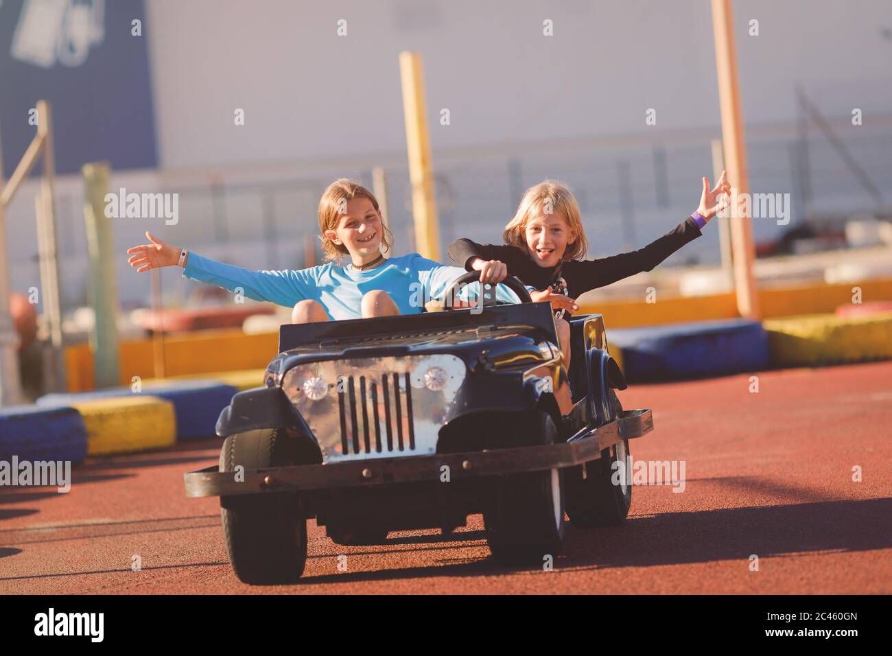 Junge Mädchen, die an einem sonnigen Tag in einem elektrischen Spielzeugauto in einer Küstenregion fahren Stockfoto
