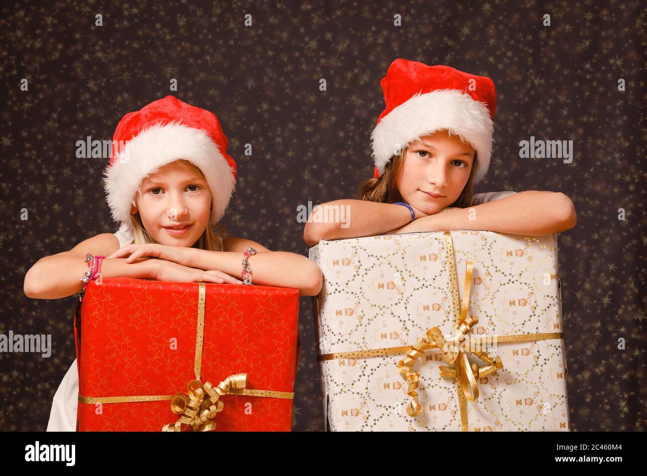 Zwei junge Mädchen, im Alter von 8-12 Jahren, tragen Weihnachtsmützen, halten Weihnachtsgeschenke, Blick auf die Kamera Stockfoto