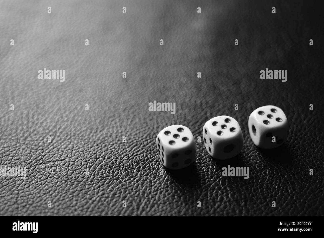 Drei Würfel mit fünf auf einem schwarzen Ledertisch in der Ecke. BW-Foto Stockfoto