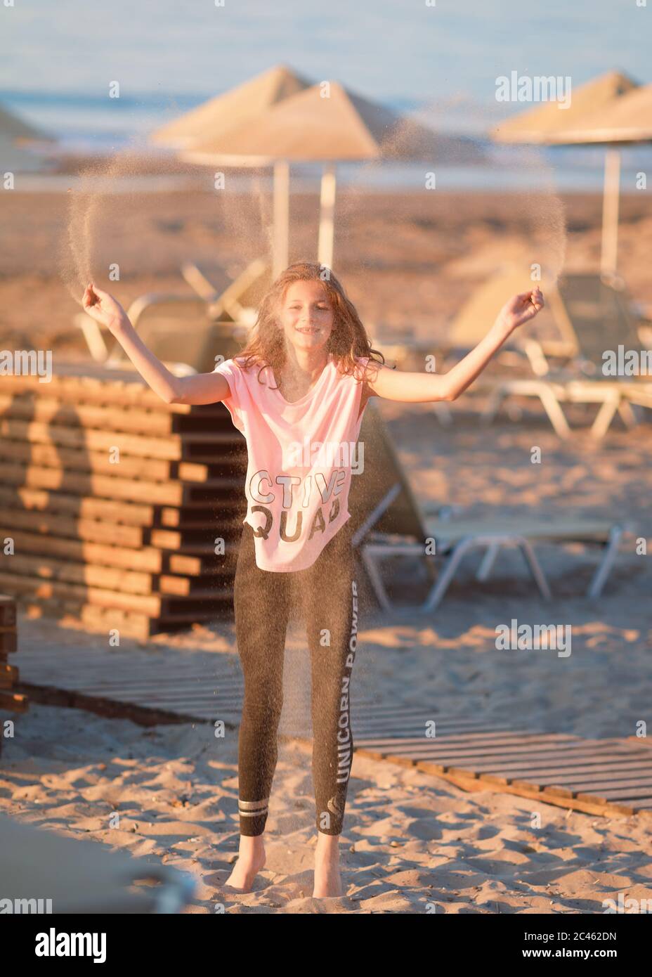 Junges Mädchen, zwischen Alter, tragen lässige Sommerkleidung, Sand in die Luft am Strand werfen Stockfoto