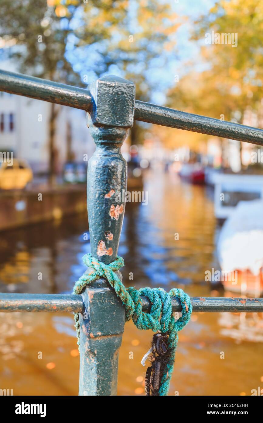 Selektiver Fokus von Green Post und Seil vor verträumtem Kanal in Amsterdam im goldenen Herbstlicht Stockfoto