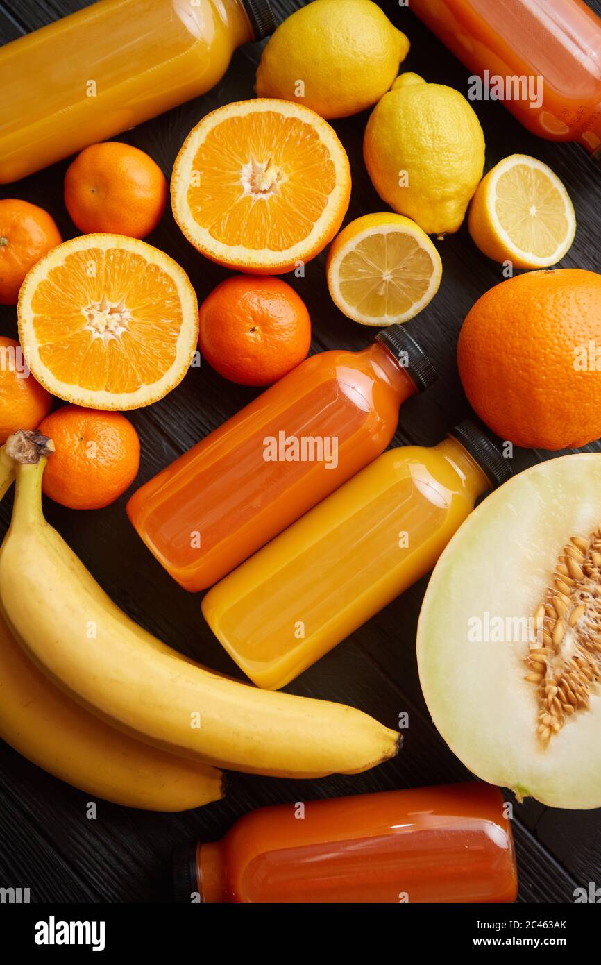 Mischung aus orangefarbenen und gelb gefärbten Früchten und Säften auf schwarzem Holzhintergrund Stockfoto