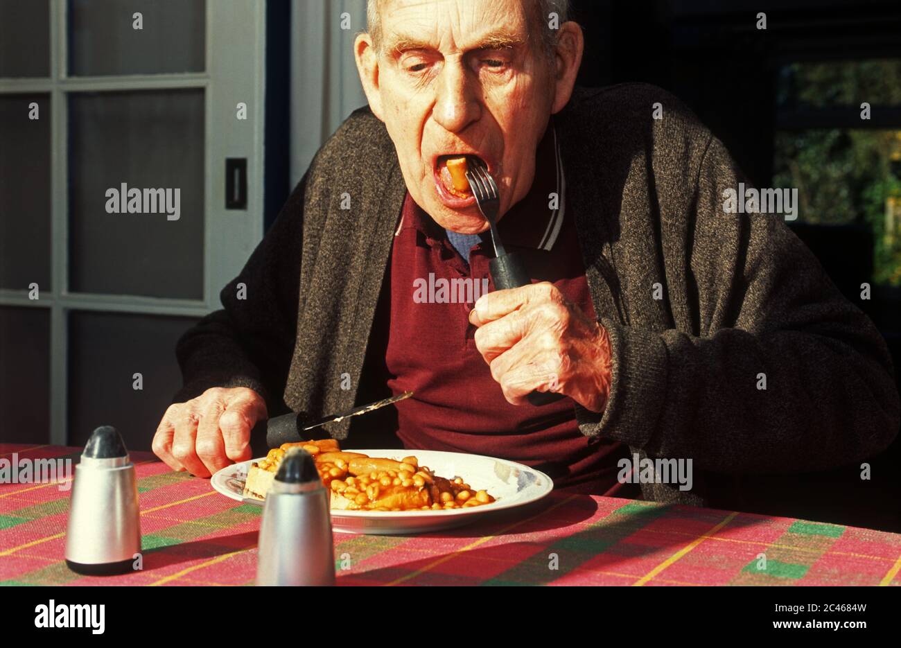 Rentner im Alter, der zum Frühstück gebackene Bohnen und Würstchen isst Stockfoto