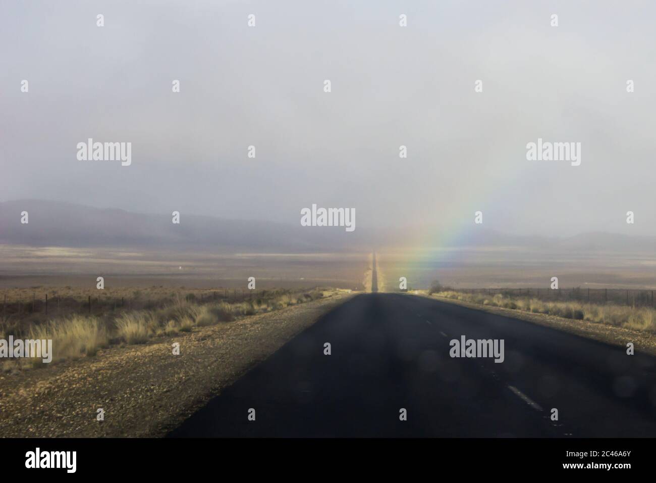 Ein Regenbogen auf der Straße vor uns nach einem schnellen Regenschauer, etwas außerhalb von Sutherland in der Karoo, Südafrika Stockfoto