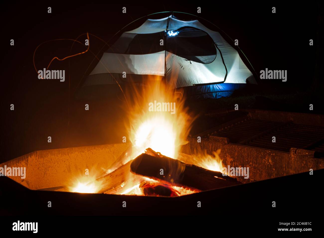 Brennendes Lagerfeuer vor einem beleuchteten Zelt in der Nacht. Stockfoto