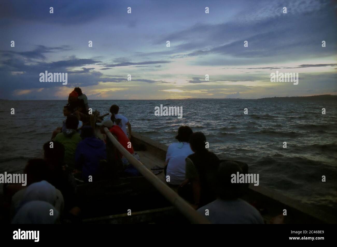 Passagiere genießen die Meereslandschaft während der Dämmerung auf dem Meer, während ein Holzboot auf der Sundastraße fährt. Die Panaitan Insel ist auf der rechten Seite zu sehen. Eine Seerundfahrt während der Regenzeit zwischen dem Ujung Kulon Nationalpark und Sumur Stadt in der Provinz Banten, Indonesien. Stockfoto