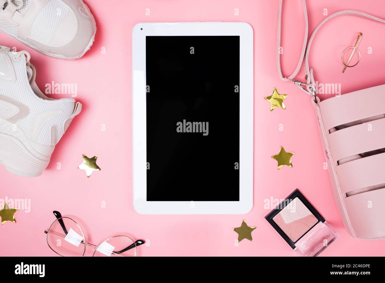 Tablet-Mock-up auf dem rosa Hintergrund mit femininem Outfit und Make-up, Draufsicht. Stockfoto