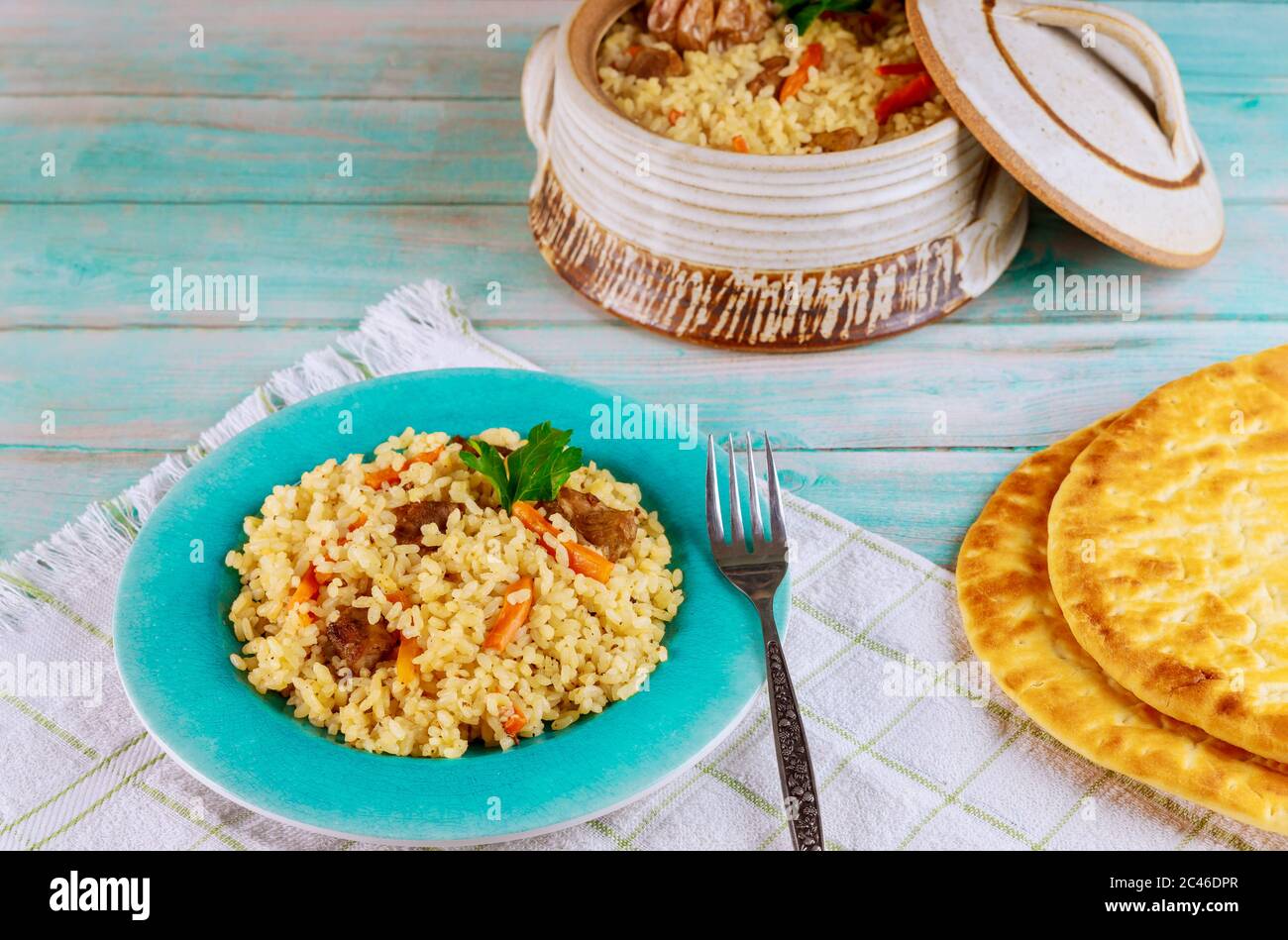 Usbekischer Reis mit Fleisch, Karotten und Knoblauch in Tontopf mit Fladenbrot. Stockfoto