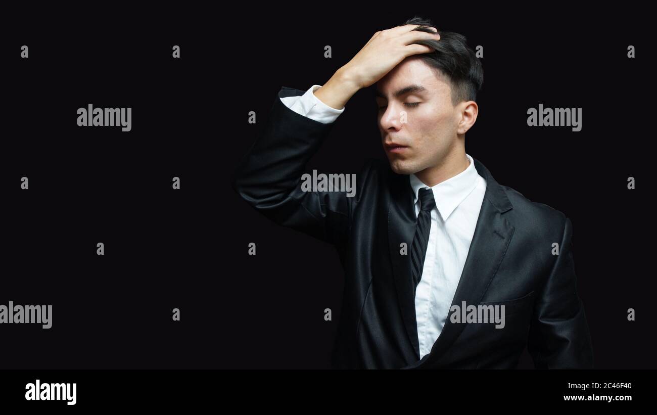 Junger latein in schwarzem Anzug, weißes Hemd, schwarze Krawatte in der  Haltung der Sorge mit der Hand auf der Stirn auf schwarzem Hintergrund  Stockfotografie - Alamy