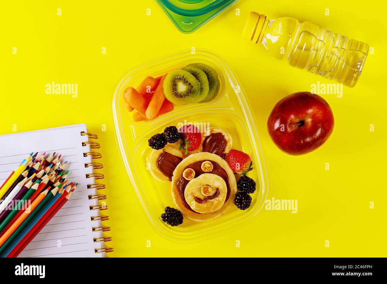 Leckeres Essen im Behälter und bunte Stifte auf gelbem Hintergrund. Zurück zur Schule Konzept. Stockfoto