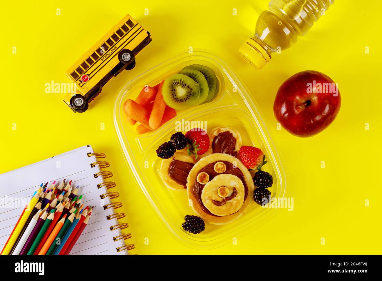 Kinder Lunchbox mit Pfannkuchen, Beeren und Apfel auf gelbem Hintergrund. Zurück zur Schule Konzept. Stockfoto