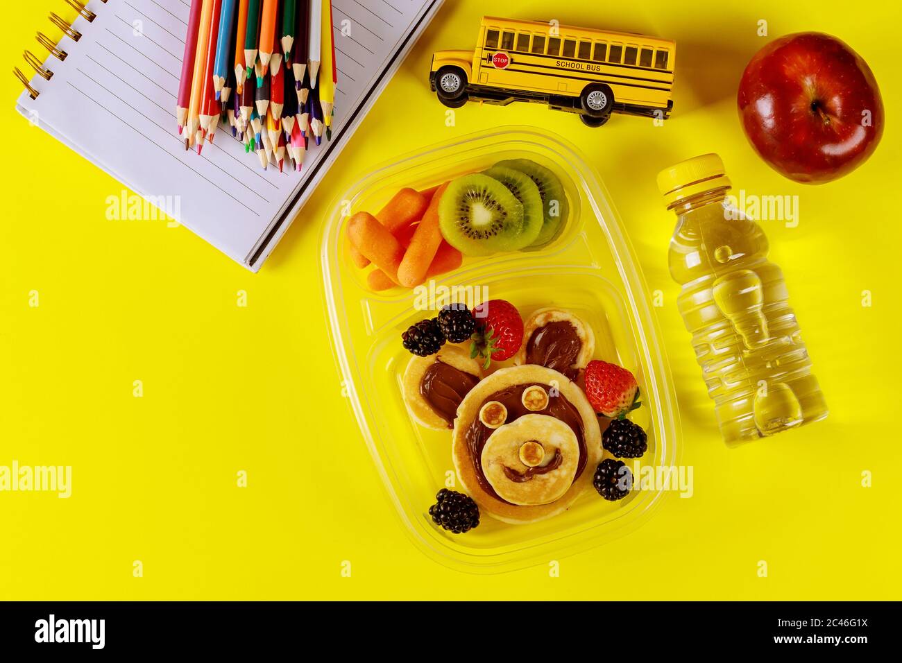 Kinder Lunchbox mit Pfannkuchen, Beeren, Getränk und Apfel auf gelbem Hintergrund. Zurück zur Schule Konzept. Stockfoto