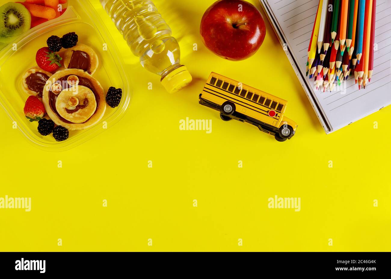 Leckeres Essen im Behälter und bunte Stifte auf gelbem Hintergrund. Zurück zur Schule Konzept. Stockfoto