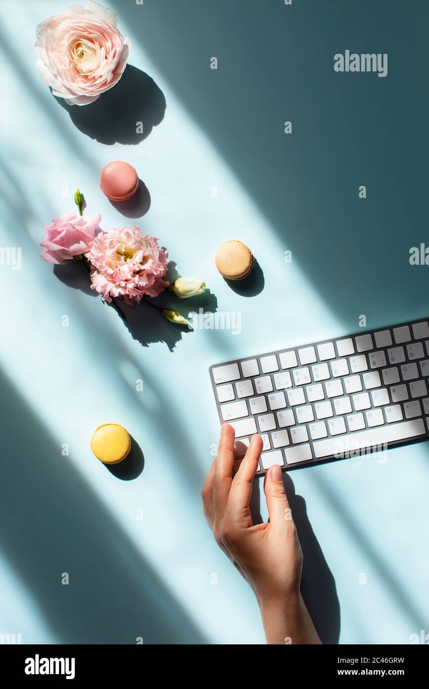 Arbeitsplatz zu Hause am Fenster. Flacher Lat mit Makronen im Sonnenlicht und einer Frau Hand tippen auf der Tastatur. Stockfoto